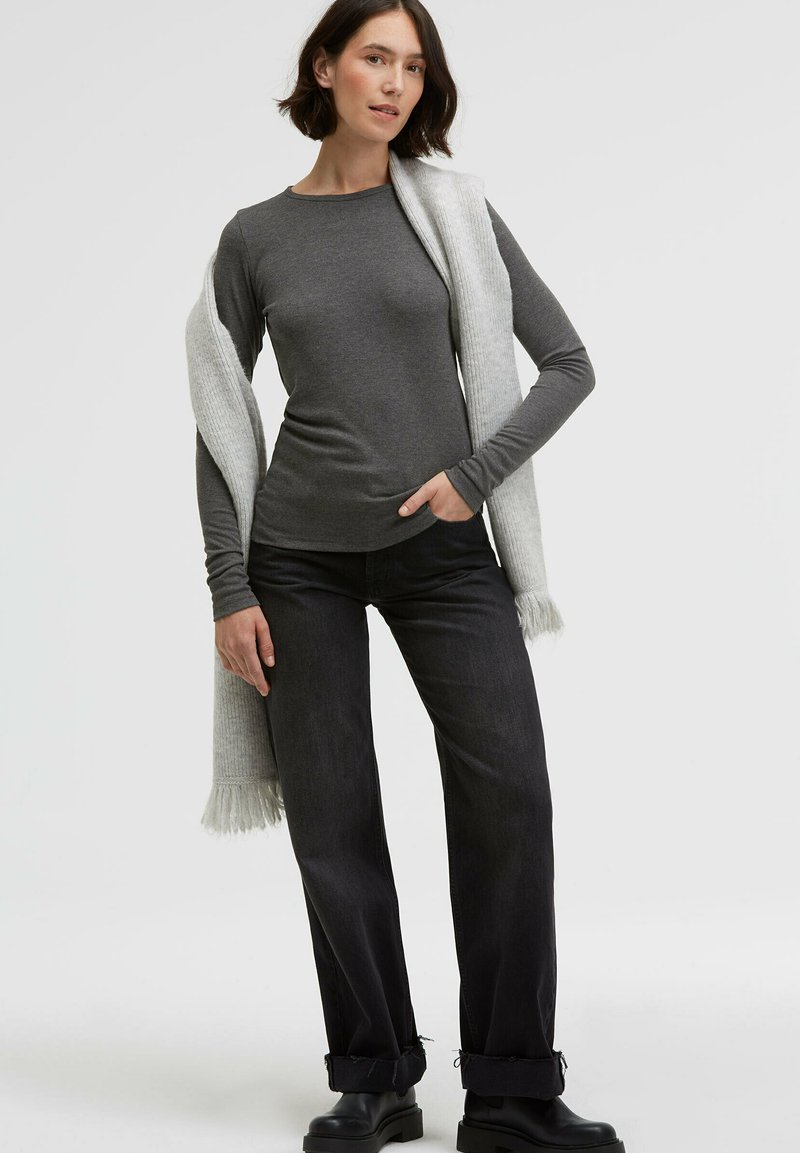 Gray long-sleeve top paired with dark jeans, draped light gray scarf, and black ankle boots. Casual fit with ribbed texture on scarf.