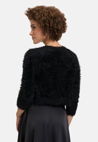 Schwarze, fuzzy, kürzere Strickjacke mit langen Ärmeln und einem runden Ausschnitt. Weicher Stoff, minimalistische Details und ein offener Rücken.