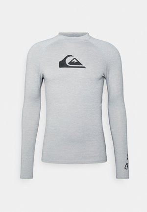 Light grey long-sleeve rash guard made of stretch fabric. Features a black logo on the chest and contrasting stitching along the seams.