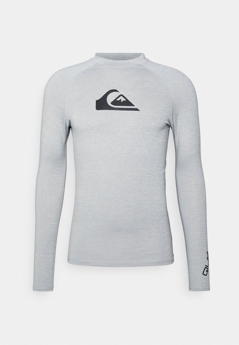Svetlo šedý dlhý rukáv rash guard vyrobený z elastickej tkaniny. Disponuje čiernym logom na hrudi a kontrastným šitím pozdĺž švov.
