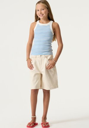 Camiseta sin mangas a rayas en azul y blanco, combinada con shorts beige. Los shorts tienen bolsillos delanteros. El calzado son chanclas rojas.