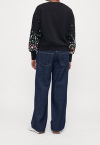 Sweat-shirt noir avec broderie florale sur les manches, associé à un jean bleu à jambes larges. Design simple ; tissu doux avec poignets et ceinture côtelés.