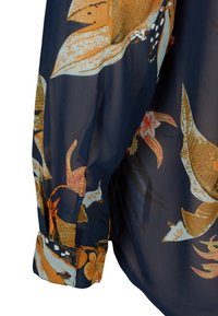 Blouse transparente bleu marine à motifs floraux avec accents orange et crème. Dotée d'un poignet boutonné et d'un tissu léger et texturé.