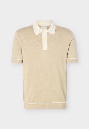 Tricou polo bej cu mâneci scurte, guler alb, deschidere cu trei nasturi și manșete și tiv striate cu o bordură subtilă albă.