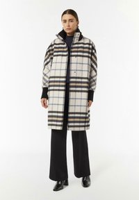 Karierten Mantel in Creme-, Schwarz- und Blautönen. Dickes Gewebe mit großem Kragen und Druckknopfverschlüssen, kombiniert mit schwarzen weit geschnittenen Hosen und High Heels.