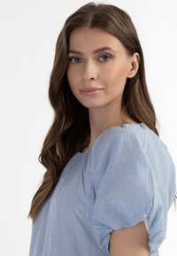 Jasnoniebieska bluzka w paski z bufkami, z okrągłym dekoltem i delikatnym marszczeniem. Wykonana z miękkiego, teksturowanego materiału.