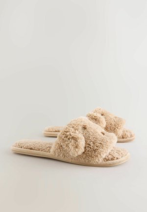 Beige fluffy slippers with a soft texture, open-toe design, and molded beige soles. Features plush fabric and rounded, textured accents.