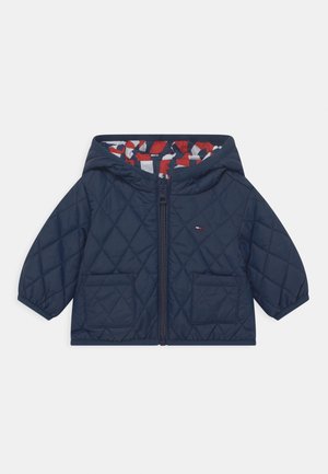 Veste matelassée à capuche bleu marine avec fermeture éclair devant, deux poches et une doublure à motifs rouge, blanc et bleu marine à l'intérieur de la capuche.
