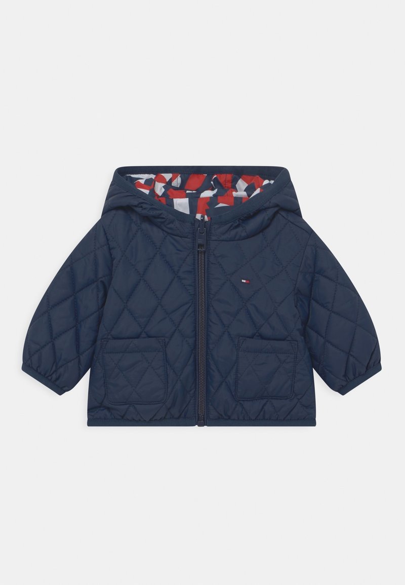 Veste matelassée à capuche bleu marine avec fermeture éclair devant, deux poches et une doublure à motifs rouge, blanc et bleu marine à l'intérieur de la capuche.