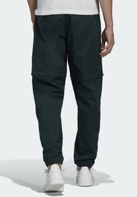 Pantaloni jogger verde scuro, a vestibilità comoda, realizzati in tessuto morbido, con polsini elastici e un design minimalista. Indossati con sneaker bianche.