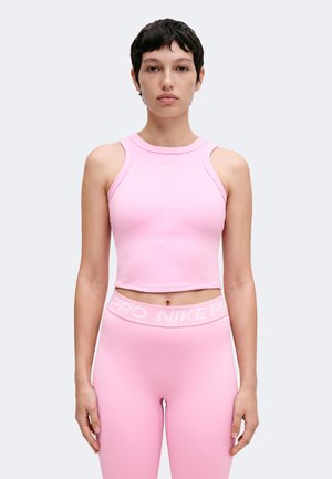 Žena s kratkom tamnom kosom u ružičastom Nike bezrukom crop topu i odgovarajućim visokim tajicama na jednobojnoj svijetloj pozadini.