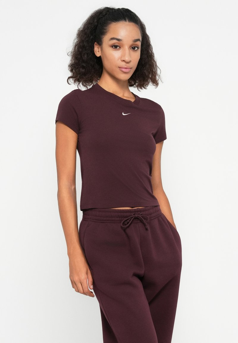 Maglietta corta bordeaux, maniche corte, scollatura rotonda, con logo Nike bianco sul petto. Abbinata a pantaloni da jogging bordeaux coordinati.