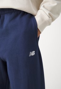 Tamne plave trenirke napravljene od mekanog materijala, sa elastikom u struku i malim bijelim logotipom New Balance s bočne strane.