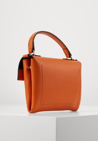 Piccola borsa a tracolla in pelle arancione con finitura strutturata, forma quadrata e manico corto. Presenta bordature nere e un design semplice e pulito.