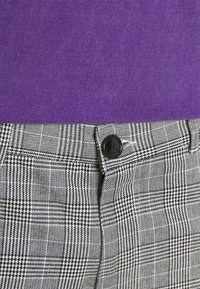 Black and white plaid trousers with a visible black button and zipper, paired with a solid purple top in a soft texture.