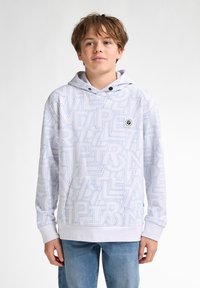 Witte hoodie met blauwe geometrische tekstpatronen, koordjes in de capuchon, ribgebreide manchetten en onderkant. Draagt met lichtblauwe spijkerbroek.