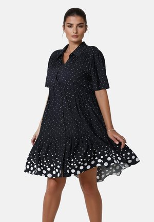 Black polka dot dress with short sleeves, button front, and a tiered, flared hem featuring large white dots at the bottom. Soft fabric texture.