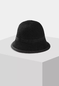 Czarna dziergana czapka typu bucket z teksturowanym wzorem i wąskim rondem, prezentowana na białym sześcianie na jednolitym tle.