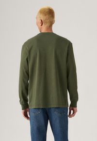 Olijfgroene katoenen t-shirt met lange mouwen, een ronde hals en een losse pasvorm, gecombineerd met blauwe jeans. Eenvoudig en minimalistisch ontwerp.