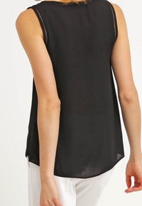 Top nero senza maniche con una texture liscia, caratterizzato da un orlo curvo e dettagli cuciti sul collo.