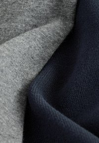 Detailný záber na jemne zloženú pleteninu v šedých a tmavomodrých farbách, ktorý zobrazuje textúru a jemné detaily šitia.