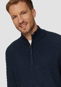Dunkelblauer Strickpullover mit strukturiertem Rautenmuster, Stehkragen und Reißverschluss am Hals. Aus weichem Material, ideal zum Layering.