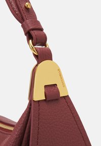 Bordeaux leren tasriem met een gestructureerde afwerking, voorzien van een gouden metalen hardware detail en logoaccent voor een veilige bevestiging.