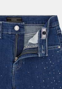 Donkerblauwe denim jeans met een rits, knopenluiting en zilveren studs die de voorkant accentueren. De textuur van de stof lijkt glad en stevig.
