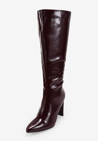 Botas hasta la rodilla, de puntera afilada en cuero burdeos brillante, con un diseño ajustado y tacón ancho para mayor estabilidad. Textura suave, detalles mínimos.