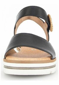 Sandale en cuir noir avec deux larges brides et un accent tressé sur le côté. Semelle intérieure texturée, avec une semelle extérieure blanche superposée.