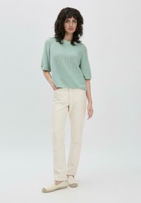 Pull en maille texturée vert menthe à manches courtes, assorti à un pantalon droit couleur crème et des chaussures slip-on beiges.