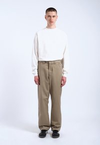 Witte langemouw shirt en beige broek, de broek heeft een ontspannen pasvorm, een platte voorkant met riemlussen, gecombineerd met zwarte sneakers.