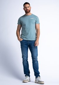 Een lichtblauwe t-shirt met ronde hals en korte mouwen, gecombineerd met donkere jeans en witte sneakers. Eenvoudig ontwerp, zachte stof, minimaal merklogo.