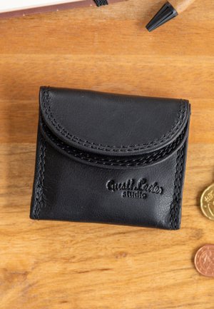 Bolsa de monedas de cuero negro con costuras visibles y logo "Quailr Leder studio" en relieve sobre una superficie de madera con monedas cerca.