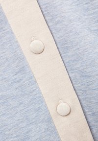 Hellblauer Stoff mit einer weichen Textur verfügt über eine beige Knopfleiste, die runde, mit Stoff bezogene Knöpfe zeigt, die gleichmäßig entlang der Naht angeordnet sind.