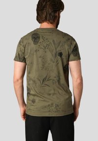 T-shirt vert olive en coton, avec des imprimés floraux noirs et des crânes. Coupe classique avec manches courtes et col rond.