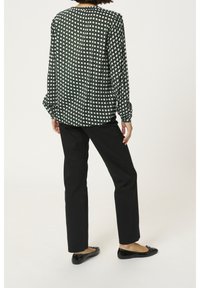 Langärmlige Bluse im schwarz-weißen geometrischen Muster, mit lockerer Passform und gerafften Bündchen, kombiniert mit schwarzen schmalen Hosen und flachen Schuhen.