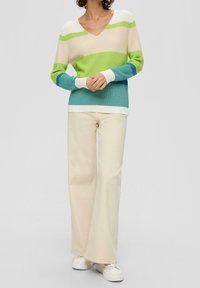 Kolorowy sweter dzianinowy z dekoltem w serek; ma naprzemienne paski w kolorze zielonym, niebieskim i kremowym. Połączony z kremowymi spodniami w szerokim kroju i białymi sneakersami.