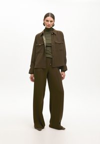 Completo a due pezzi verde oliva composto da una camicia con bottoni e tasche sul petto e pantaloni a gamba larga. Texture morbida, vestibilità sartoriale, design minimalista.