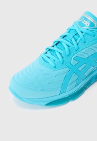 Tirkīza krāsas sporta kurpe ar teksturētu augšdaļu, tīkliņa paneļiem un gumijas zolīti. Aprīkota ar austām šņorēm un raksturīgu zīmola logotipu.