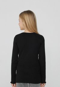 Czarny sweter z długim rękawem, wykonany z prążkowanego materiału, z okrągłym dekoltem i falbaniastym wykończeniem. Materiał wydaje się być miękki o gładkiej fakturze.