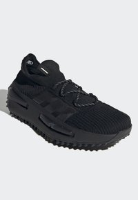 Black athletic shoe with a knitted upper, textured surface, elastic collar, and lace closure. Features a thick, rubberized sole with traction.