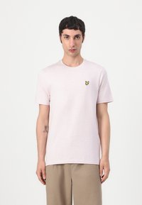 T-shirt en coton rose pâle avec des manches courtes, un col rond et un petit logo de papillon jaune sur la poitrine gauche. Design simple.