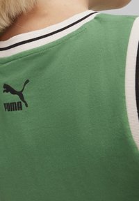 Maglietta sportiva verde in tessuto con girocollo a coste bianche e nere. Presenta un logo Puma nero sulla parte superiore della schiena. Superficie morbida e texturizzata.