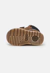 Brun mockaskinn och nät sko sula med gummigrepp, strukturerad mönster och varumärkesdetalj. Har en rundad häl och vertikala spårlinjer.