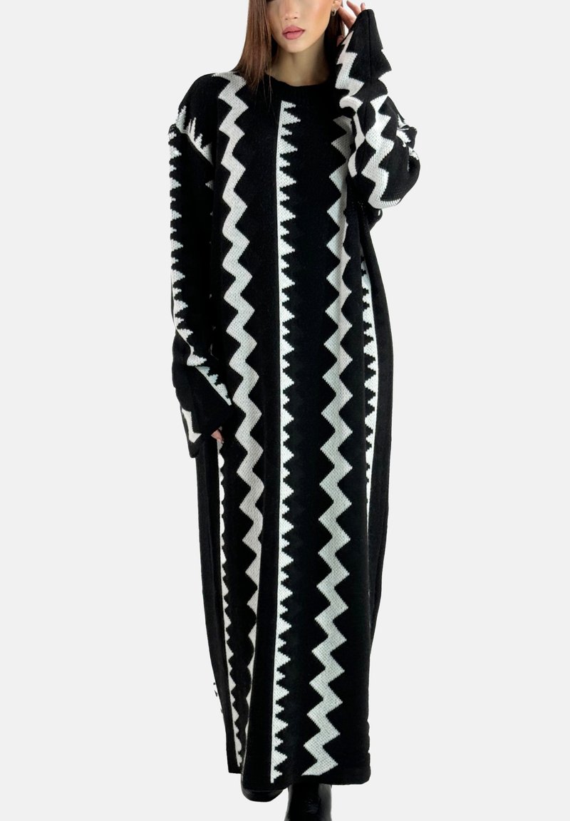 Robe longue en tricot présentant un motif zigzag noir et blanc, avec des manches larges et une silhouette droite, tissu texturé, et un col rond.