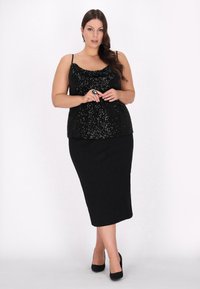 Sort sequined top med en scoop-udskæring, parret med en sort blyantskørt. Outfittet har justerbare spaghetti-stropper og er komplementeret af sorte hæle.