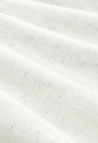 Tessuto di cotone bianco con macchie azzurro chiaro, con una superficie strutturata e un motivo di tessitura visibile. Il materiale appare morbido e resistente.