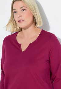 Violetti pitkähihaine pusero, jossa on V-pääntie, valmistettu pehmeästä, teksturoidusta kankaasta. Ominaisuuksia rento istuvuus ja minimaaliset ompeluyksityiskohdat.