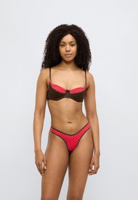Σετ μπικίνι καφέ και κόκκινο με πουά, διαθέτοντας στηθόδεσμο με δομημένο σχεδιασμό και λεπτομέρεια φιόγκου μπροστά, και σλιπ με ψηλό κόψιμο.